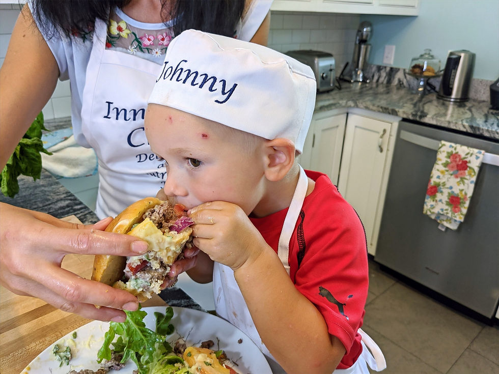 A mother helping her young son hold a hamburger that he's eating