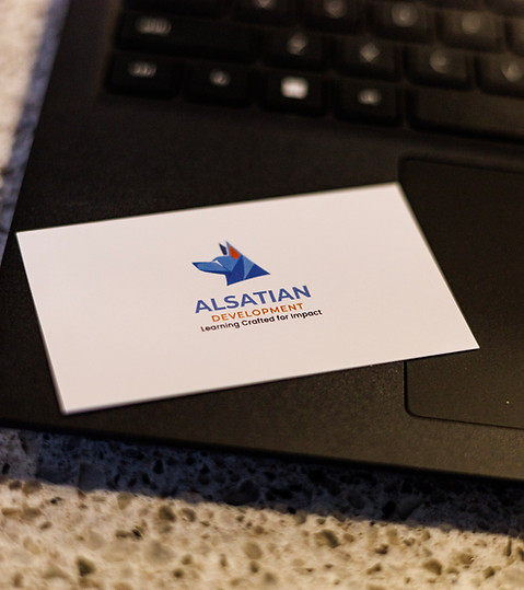 Alsatian Development business card featuring a blue geometric dog logo and the tagline ‘Learning Crafted for Impact,’ placed on a laptop keyboard.