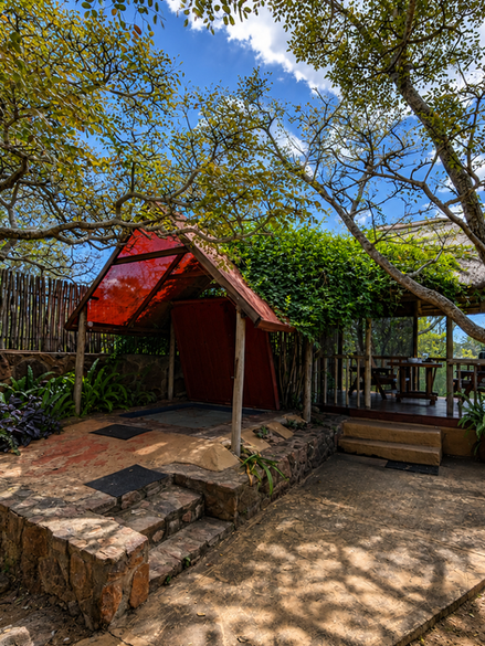 Covered and cozy warm water jacuzzi (hot tub) with lush green next to a covered outdoor dining area and braai boma