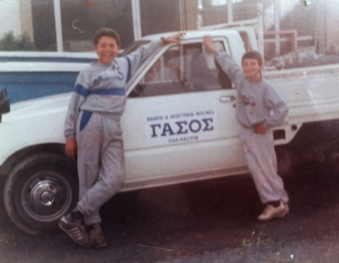 Two smiling boys leaning on a white "ΓΑΣΟΣ" wood delivery truck.