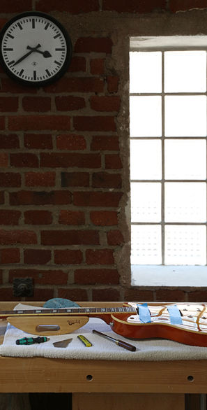 Les Paul E-Gitarre auf der Werkbank vor einer Ziegelwand mit Fenster aus Glasbausteinen