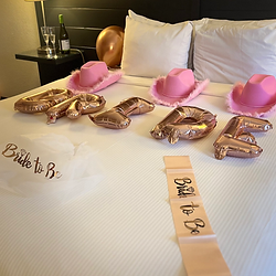Bride balloons and sash laid out on the bed for a hotel room bachelorette room set up