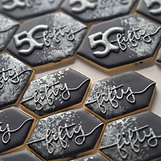 an array of elegantly decorated 50th birthday custom cookies, black with silver touches. some have the number "50" with the word "fifty" written through the "0" and others with the word "fifty" written across the front