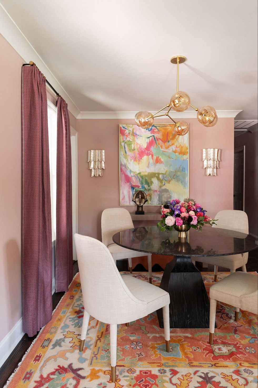Pink dining space with white chairs, dark table, and vibrant rug.