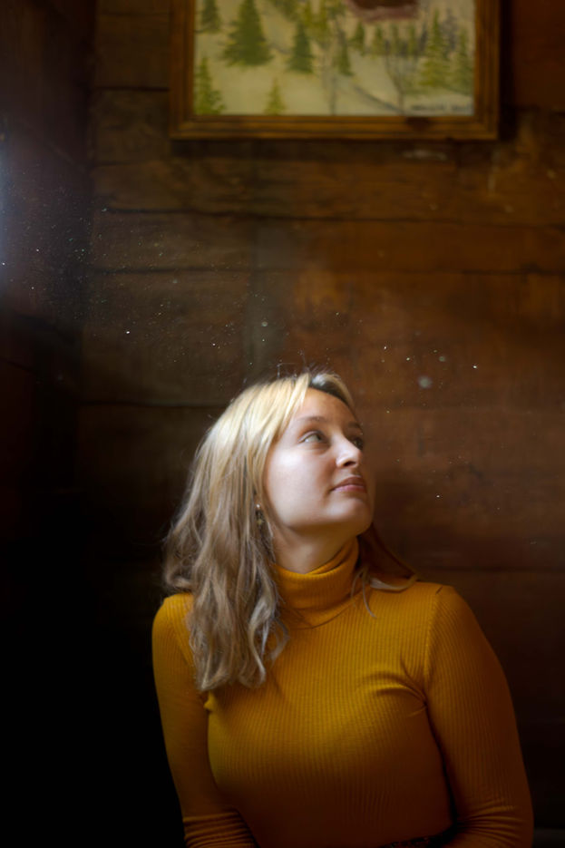 Portrait of a woman with sunlight shining on her face through a small window in a wooden bungalow