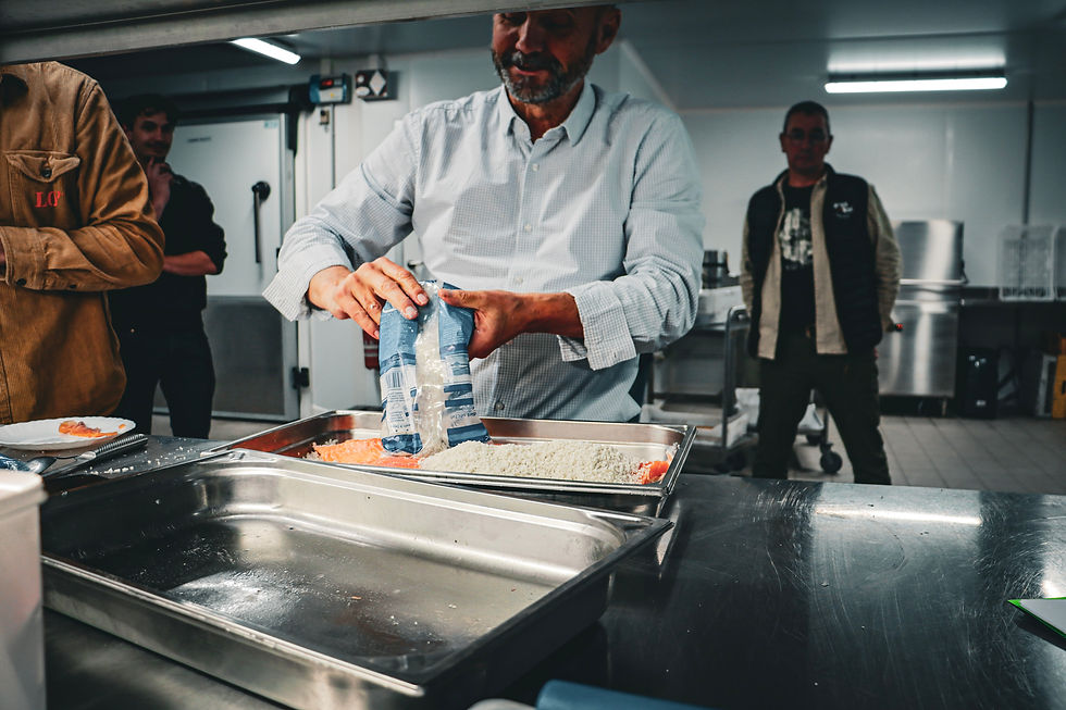 Un homme verse un sachet bleu dans un bac de cuisine inox, deux personnes regardent en arrière-plan sous néons.