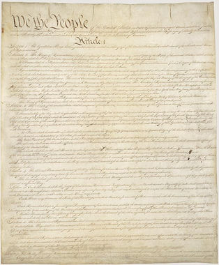 A faded photograph of the US constitution written in script; the image is decorative and the words are illegible except "We the People" at the top.