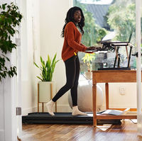 Woman working standing on treadmill with laptop, looking focused, in home office