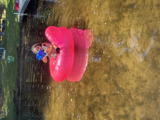 Girl on pink innertube swimming in the lake.
