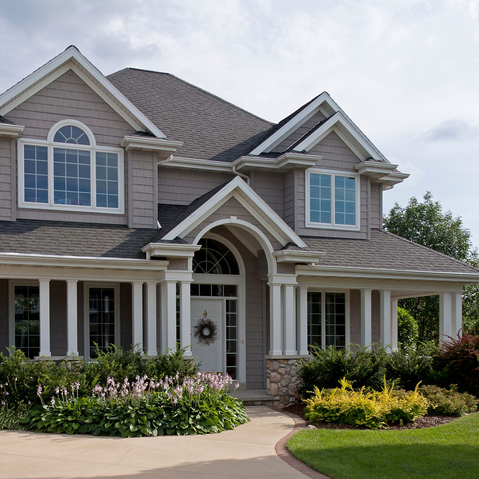 Elegant suburban home exterior with grey siding, large windows, covered porch, landscaped