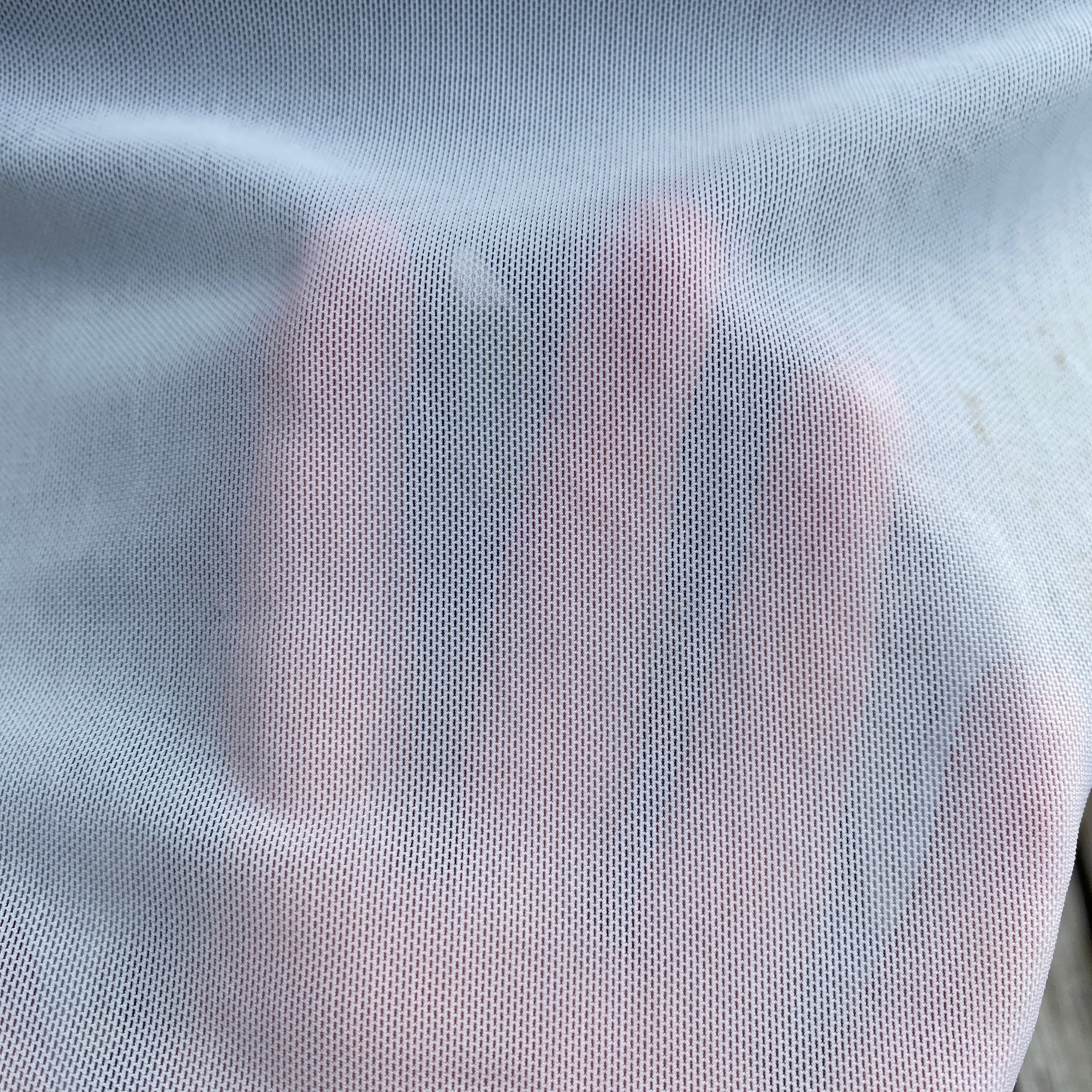 Close-up of warm white mesh fabric with hand underneath showing colour and transparency