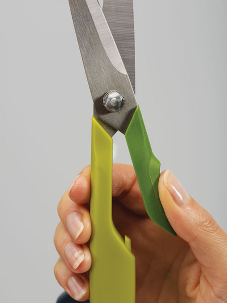 Open Twin Cut scissors held in a user's hand, showing ambidextrous functionality and mass-market product design.