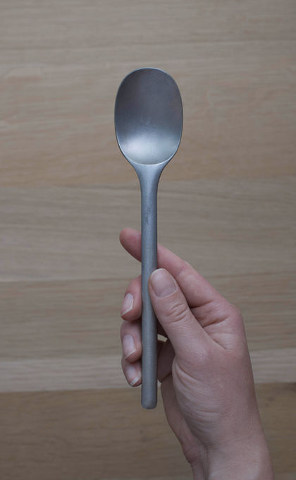 Laser-sintered metal prototype of spoon, held in hand, highlighting ergonomic design and prototype testing.