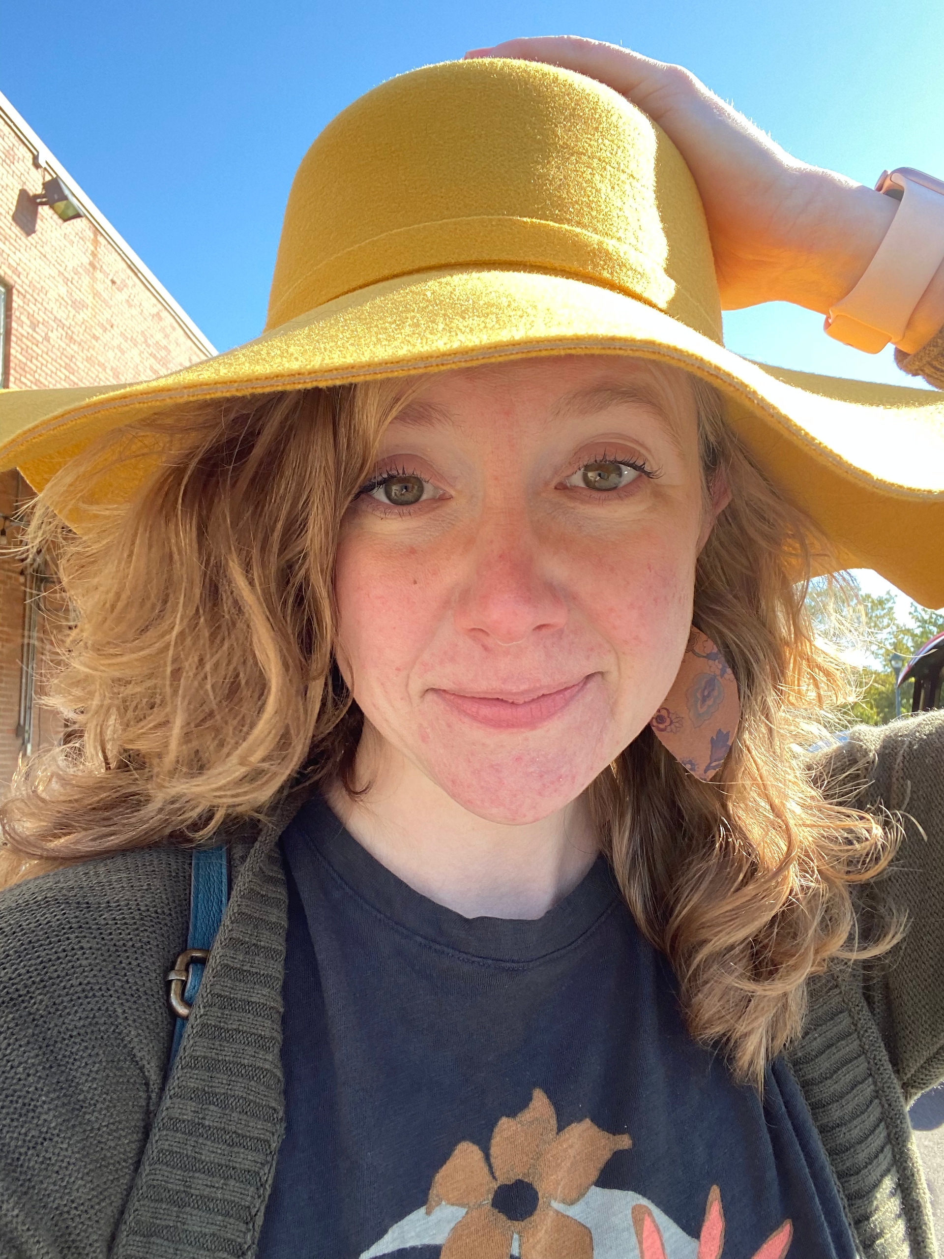 Caitlin with wavy dark blond hair down and a yellow hat on a sunny day