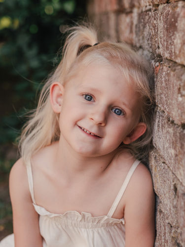 Einfühlsame Kindergartenfotografie: Ein Kind sitzt lächelnd auf einer Holzbank im Freien, Kitafotografin aus Grefrath fotografiert in Kitas in Nettetal, Viersen, Krefeld und Mönchengladbach – auch für neurodivergente Kinder.