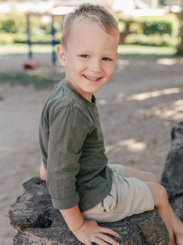Einfühlsame Kindergartenfotografie: Ein Kind sitzt lächelnd auf einer Holzbank im Freien, Kitafotografin aus Grefrath fotografiert in Kitas in Nettetal, Viersen, Krefeld und Mönchengladbach – auch für neurodivergente Kinder.