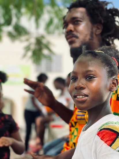 Ras Richie of Humble and Free wadadli playing drums while student looks on/