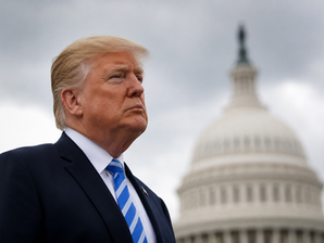 Donald Trump con traje oscuro y corbata azul, serio, ante el Capitolio de fondo borroso bajo cielo gris.