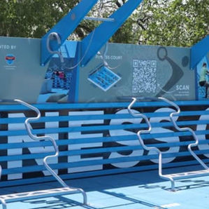 Circuito fitness azul al aire libre en Wichita, Kansas, con anillas, QR y paneles informativos bajo árboles.