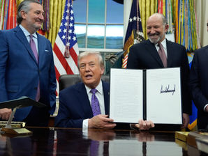 Trump muestra un documento firmado junto a tres hombres sonrientes en el Despacho Oval, con banderas de EE. UU.