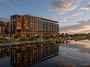 Edificio moderno junto al agua al atardecer, con reflejo en el lago, paseantes y cielo azul anaranjado.