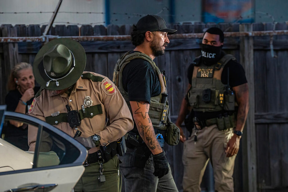 Tres agentes armados con chalecos y gorras junto a un auto blanco, en un patio cercado; uno lleva mascarilla POLICE.