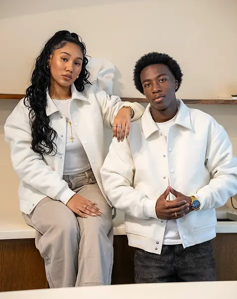 Male and female models showcasing the Verité varsity jacket. Timeless beige streetwear with luxury detailing and subtle embroidery