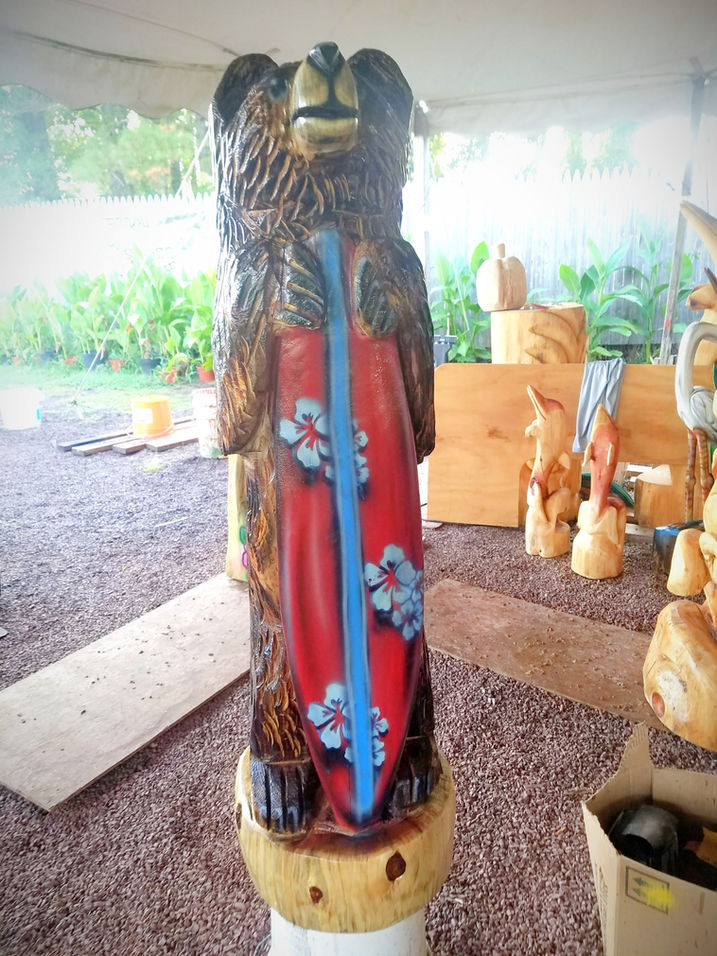 Tiki Murph chainsaw carving in white pine tall bear with red surfboard