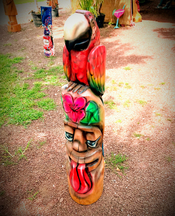 Tiki Murph carved pine double tiki with carved parrot on top, pink flower in middle and tongue face on bottom.