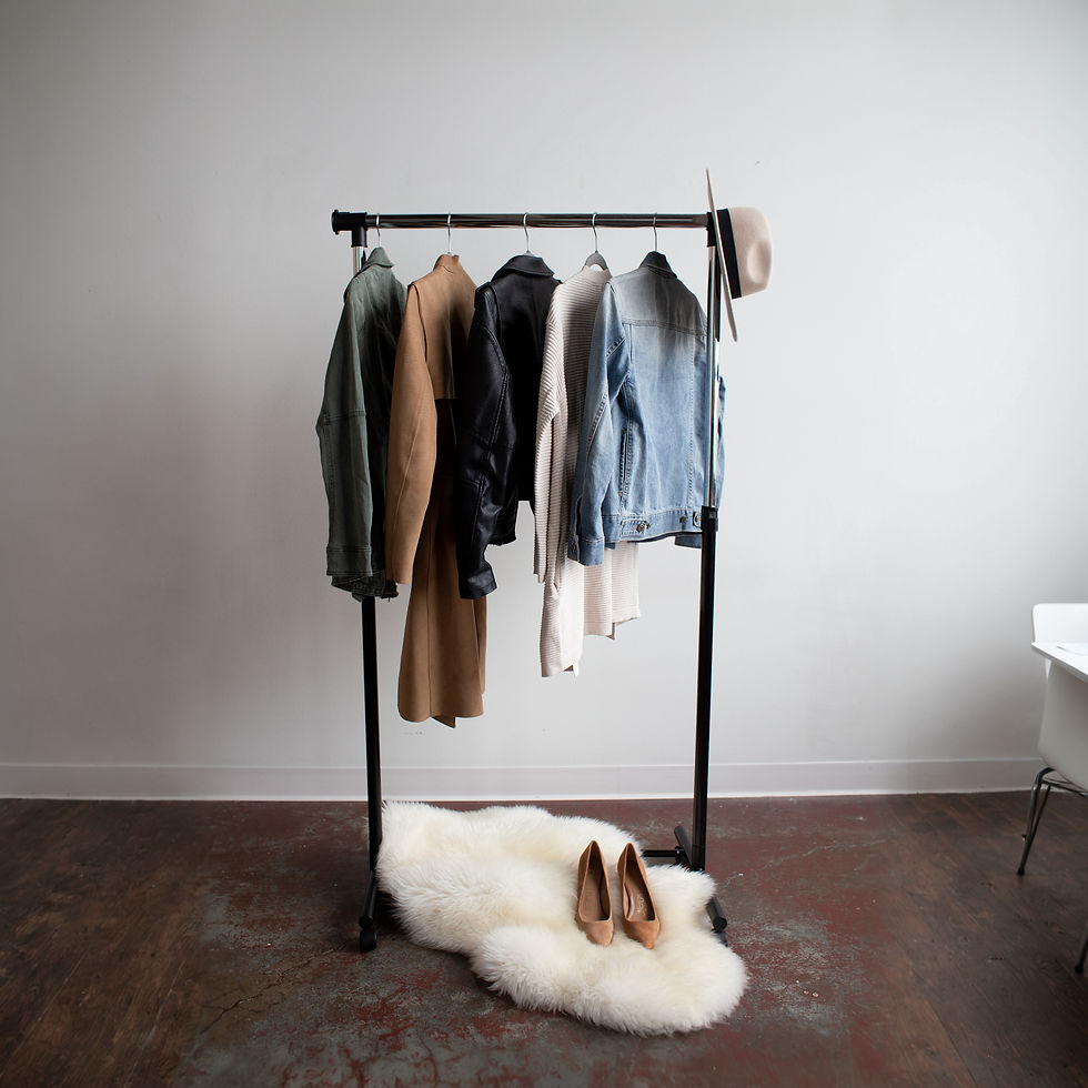Clothing rack with jackets, shirts, hat, and brown shoes on white rug. Simple capsule wardrobe. 