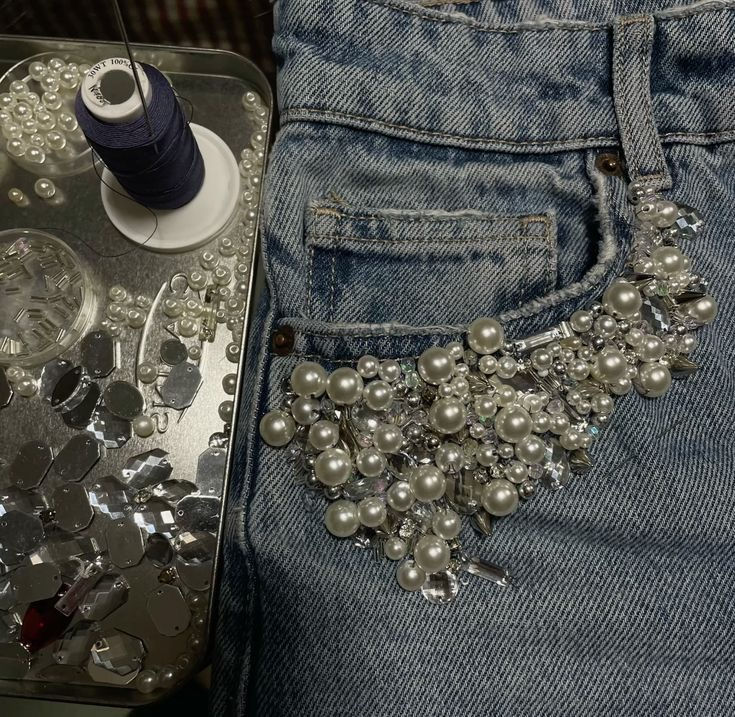 Embellished denim jeans pocket with white pearls, rhinestones, and crafting supplies.