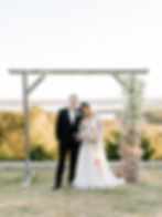 A newly married couple stands under a floral arch overlooking an Oklahoma lake