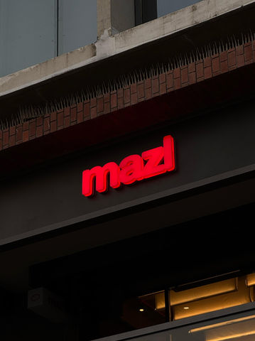  Mazl storefront sign featuring the new bright red logo mounted above the entrance.