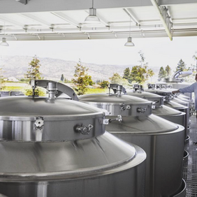 Man inspecting large stainless steel wine fermentation tanks