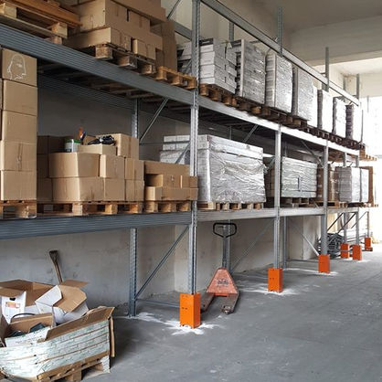 An interior view of a warehouse facility featuring multiple levels of industrial shelving units filled with various stacked boxes, containers and palletized goods.