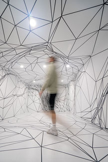 Mann läuft duch schwarzweiße Tape Art Rauminstallation aus Polygon Mustern