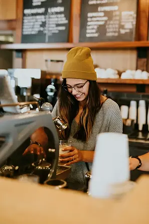 Trabajadora joven sonriente operando una máquina de café en el mostrador de una cafetería, representando el empleo cotidiano y los derechos laborales en México