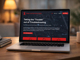 Laptop on a wooden table displaying a website for Rook System Solutions. Text: "Taking the 'Trouble' out of Troubleshooting." Warm ambient lighting.