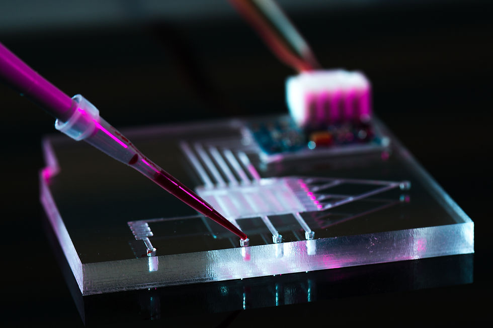 A close-up of a lab-on-a-chip device with a pipette dispensing a drop of liquid, possibly blood, onto a microfluidic chip. The image has a high-tech appearance with electronic components in the background.