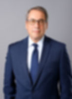 Caucasian man in blue suit photographed against a grey seamless backdrop.