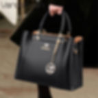 “Black structured leather handbag with top handles and gold hardware, worn by woman, elegant and sophisticated everyday bag”