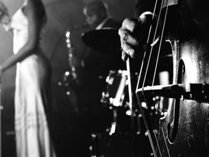 Jazz band in black and white; singer in gown at mic, saxophonist in background, close-up of bassist's hand on a double bass. Classic mood.