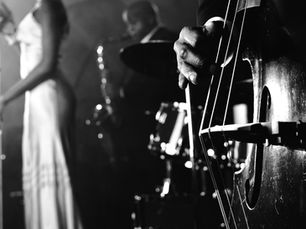 Jazz band in black and white; singer in gown at mic, saxophonist in background, close-up of bassist's hand on a double bass. Classic mood.