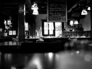 Cozy Indiranagar restaurant interior in black and white, showing tables set with glasses, a chalkboard menu, and dim lights. Peaceful atmosphere.