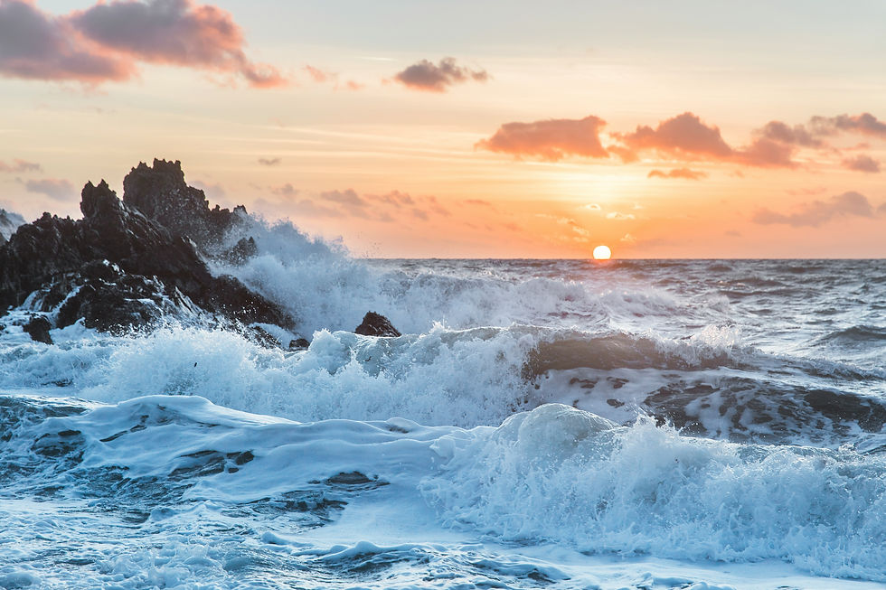Waves crash against rocks at sunset, with a vibrant orange sky and scattered clouds. The scene is dynamic and serene.