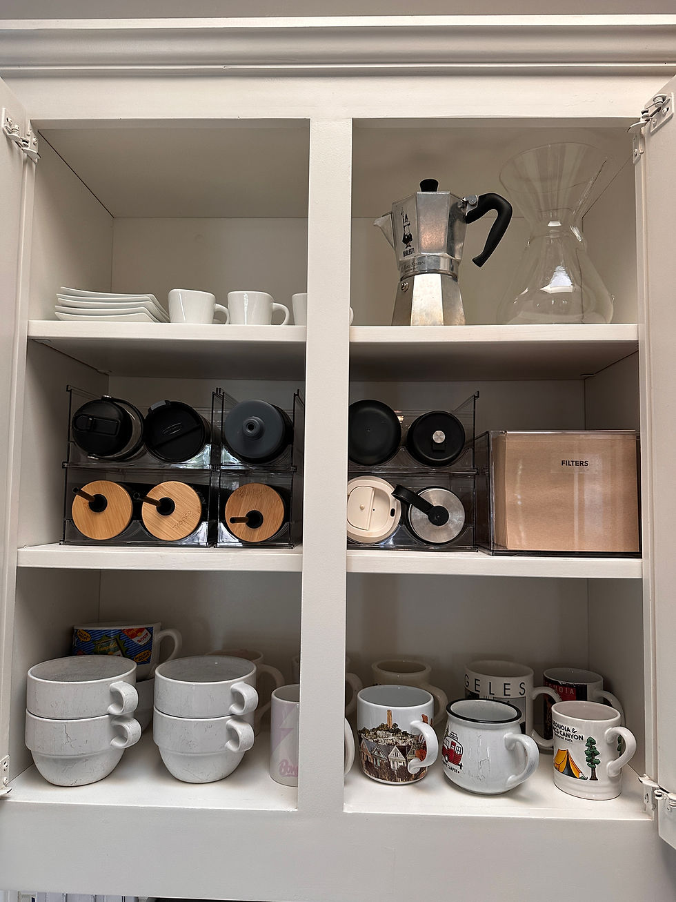 Kitchen drawer open, organized with cutlery, utensils, foil, and bags. Wooden cabinet, black cooktop, plants, and books in a bright kitchen.