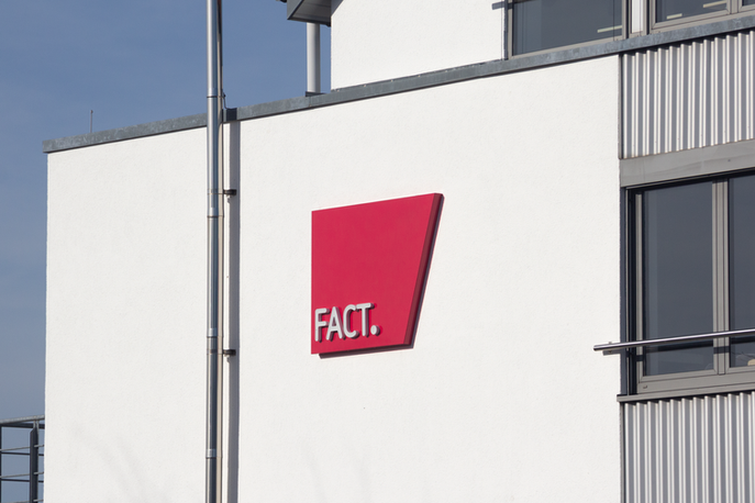 FACT.-Leuchtreklame mit Vollacrylbuchstaben und lackierter Aluhaube an einer modernen Gebäudefassade in Gesamtansicht bei Tageslicht.