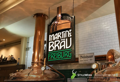 Ein Schild für das Restaurant Martins Bräu aus massiver Eiche mit aufgesetzten, gefrästen Einzelbuchstaben aus lackiertem Acrylglas. Signet aus partiell patiniertem Kupfer