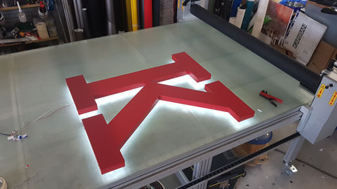 Rotes Profil 3 Rückleucht-Logo aus Alublech mit LED-Beleuchtung für Holzbau Bruno Kaiser auf Werkbank in der Produktion.