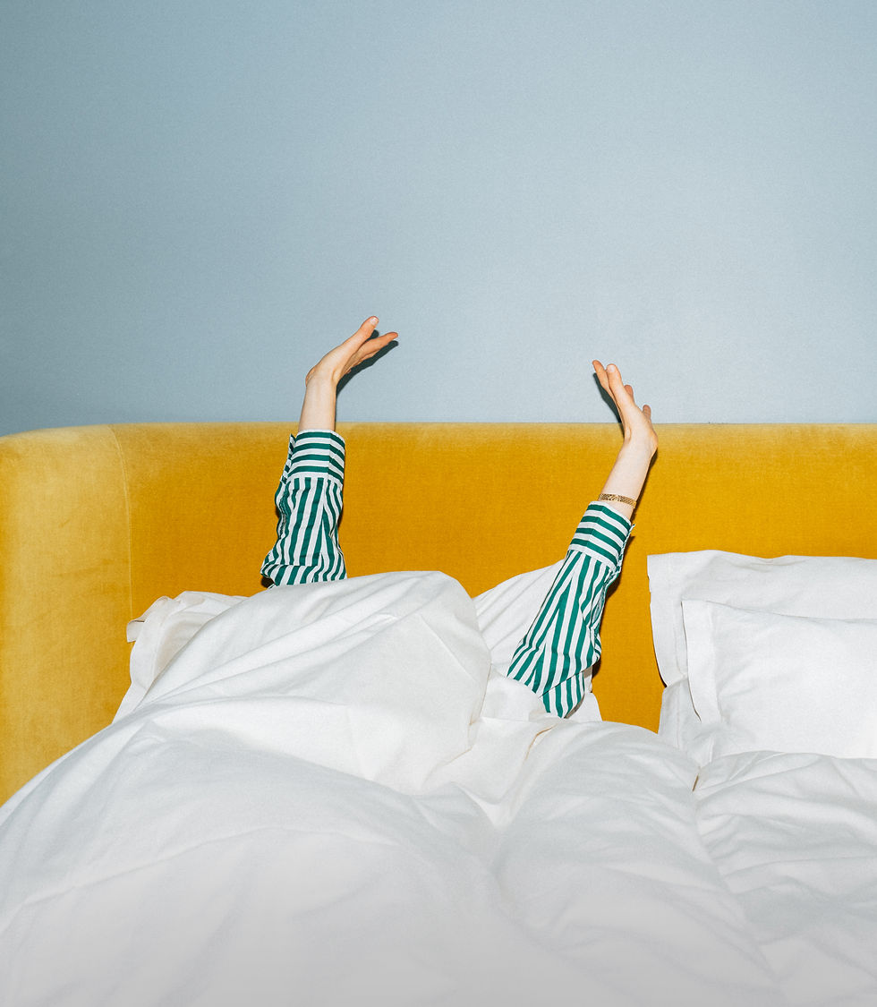 Ein Bett im stilwerk Hotel Heimhude mit einer Person in einem gestreiften Schlafanzug unter der Bettdecke die die Arme nach oben streckt